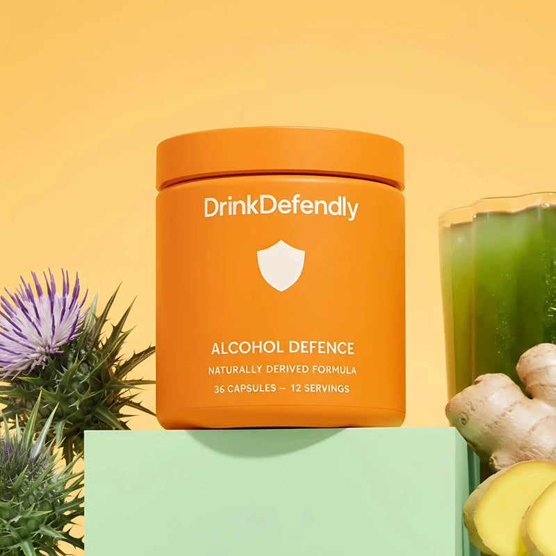 Orange container of DrinkDefendly Alcohol Defence supplement with a glass of green juice and ginger on a yellow background
